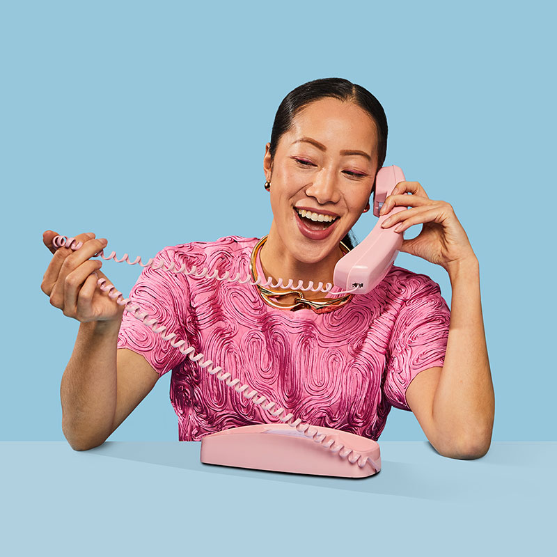 Woman talking by an Ooma Retro Pink Phone.