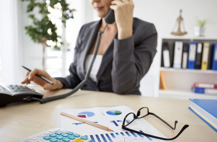 Woman sitting at a desk and dialing a call on a business phone